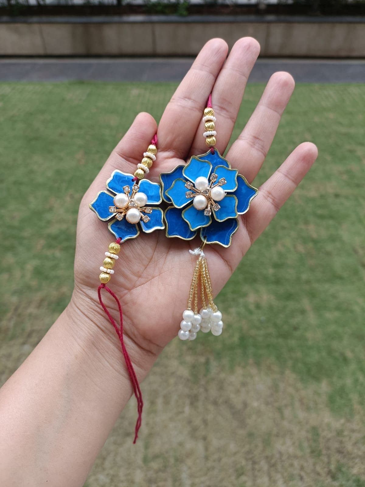 Blue floral resin rakhi with pearls and a red thread