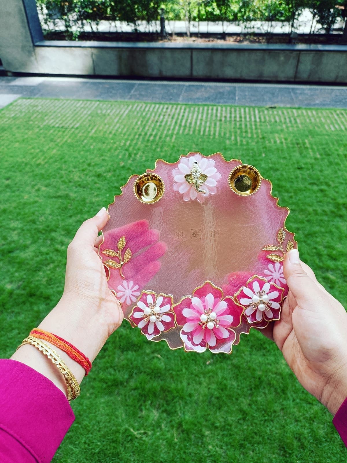 Pink resin pooja thali with flowers, two diya cups and a Ganesha charm