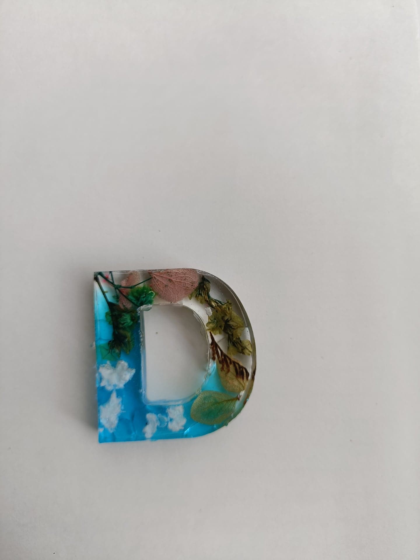 Letter D resin keychain with pressed flowers and a blue sky